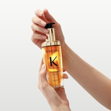 The new refillable Elixir Ultime is being held between two hands in a twist motion.